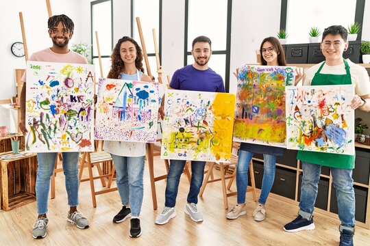 Group of young paint students smiling happy showing draw canvas standing at art studio.