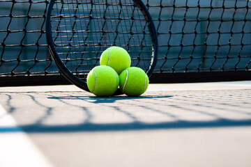 Tennis racket and three balls leaned against the net in hard court