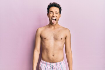 Fototapeta premium Young handsome man wearing swimwear shirtless sticking tongue out happy with funny expression. emotion concept.