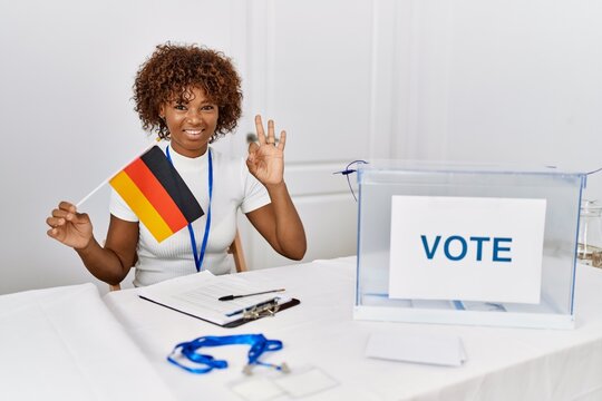 Young african american woman at political campaign election holding germany flag doing ok sign with fingers, smiling friendly gesturing excellent symbol