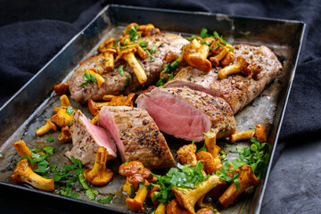 Fried dry aged pork fillet chateaubriand medallion steak natural with chanterelles and parsley served as close-up on a rustic metal tray on black background © HLPhoto