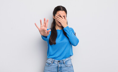 pretty young woman covering face with hand and putting other hand up front to stop camera, refusing...