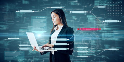 Attractive young caucasian businesswoman using laptop with abstract glowing big data blockchain interface on dark background. Cryptocurrency, finance, big data and information concept.