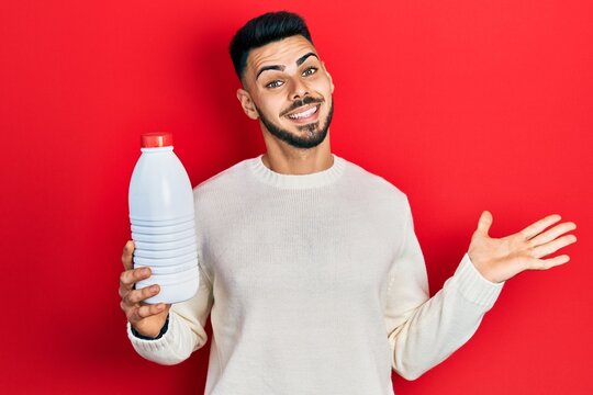 Young hispanic man with beard holding liter bottle of milk celebrating achievement with happy smile and winner expression with raised hand