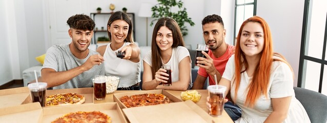 Group of young people smiling happy eating italian pizza sitting on the table at home