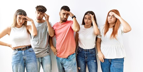 Obraz premium Group of young friends standing together over isolated background worried and stressed about a problem with hand on forehead, nervous and anxious for crisis