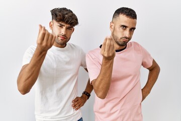 Young gay couple standing over isolated background doing italian gesture with hand and fingers confident expression