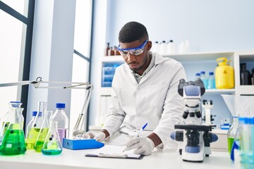 Young african american man wearing scientist uniform weighing diamond at laboratory