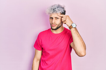 Young hispanic man with modern dyed hair wearing casual pink t shirt pointing unhappy to pimple on...