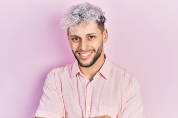 Young hispanic man with modern dyed hair wearing casual pink shirt happy face smiling with crossed arms looking at the camera. positive person.