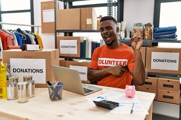 Young african man working as volunteer t shirt at donations stand smiling with happy face winking...