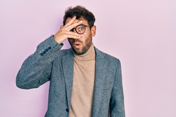 Handsome man with beard wearing business jacket and glasses peeking in shock covering face and eyes...