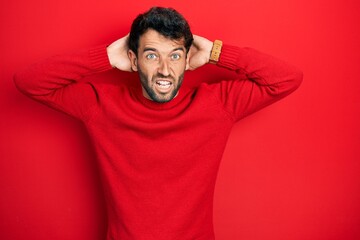 Handsome man with beard wearing casual red sweater crazy and scared with hands on head, afraid and surprised of shock with open mouth