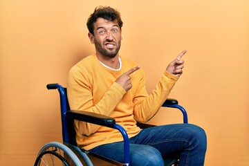 Handsome man with beard sitting on wheelchair pointing aside worried and nervous with both hands,...