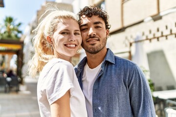 Young beautiful couple of caucasian girlfriend and hispanic boyfriend hugging in love outdoors on a sunny day. Woman and man smiling happy dating relationship