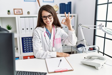 Obraz na płótnie Canvas Young doctor woman wearing doctor uniform and stethoscope at the clinic smiling positive doing ok sign with hand and fingers. successful expression.