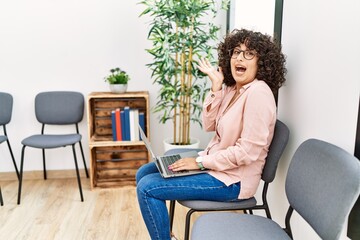 Young middle eastern woman sitting at waiting room working with laptop celebrating victory with happy smile and winner expression with raised hands