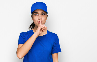 Young hispanic girl wearing delivery courier uniform asking to be quiet with finger on lips....