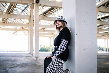 Stylish millennial woman with skateboard leaning on pillar