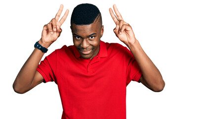 Young african american man wearing casual red t shirt posing funny and crazy with fingers on head as bunny ears, smiling cheerful