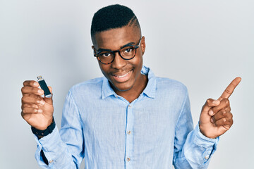 Young african american man holding removable memory usb smiling happy pointing with hand and finger to the side