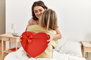 Young woman surprising her girlfriend with valentine gift at bedroom.