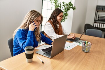 Two business workers woman talking on the smartphone and using laptop at the office.