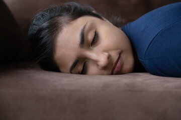 Head shot exhausted young Indian woman sleeping on couch, feeling restless after hard working day, relaxing renewing energy at home, napping daydreaming, watching sweet dreams, fatigue concept.