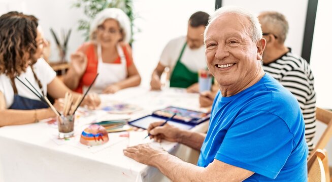 Group of middle age draw students sitting on the table drawing at art studio. Man smiling happy looking to the camera.