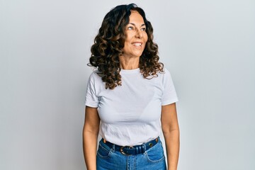 Middle age hispanic woman wearing casual white t shirt looking away to side with smile on face, natural expression. laughing confident.