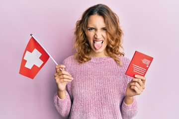 Young caucasian woman holding swiss flag and passport sticking tongue out happy with funny...