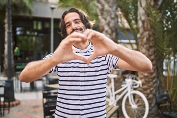 Young hispanic man with beard outdoors at the city smiling in love doing heart symbol shape with hands. romantic concept.