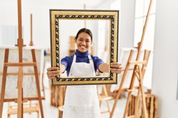 Young latin woman smiling confident holding empty frame at art studio