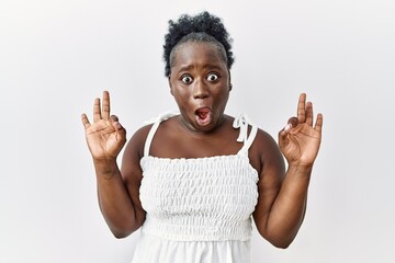 Young african woman standing over white isolated background looking surprised and shocked doing ok...