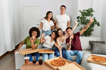 Group of young friends having party eating italian pizza and singing song at home.