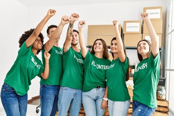 Group of young volunteers smiing happy with fists raised up at charity center.