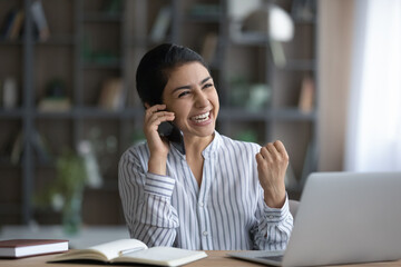 Overjoyed young Indian ethnicity woman holding phone call conversation, celebrating hearing amazing news, feeling excited getting dream job offer or opportunity, good luck success concept.