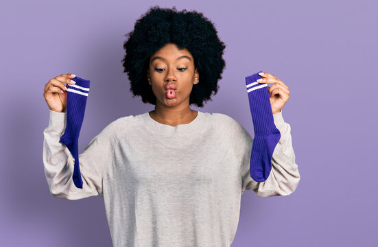 Young african american woman holding socks making fish face with mouth and squinting eyes, crazy and comical.