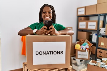 Young african american woman wearing volunteer uniform using smartphone at charity center