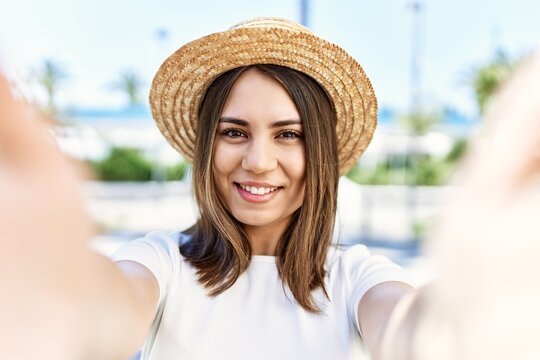 Young beautiful woman smiling happy outdoors on a sunny day wearing summer hat taking a selfie picture