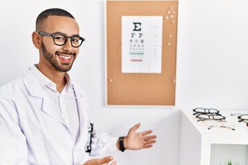 African american optician man standing by eyesight test inviting to enter smiling natural with open hand