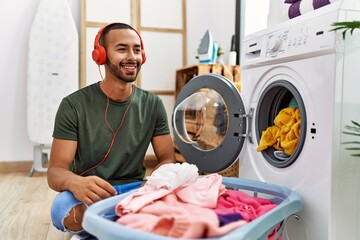 Young hispanic man listening to music using washing machine at laundry