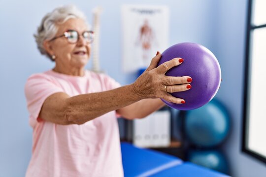Senior grey-haired woman physitherapist patient having rehab session using ball at physitherapy clinic