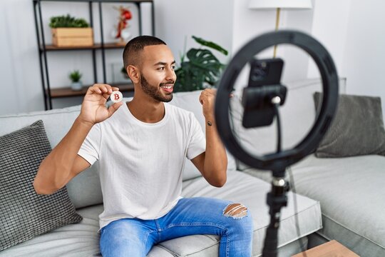 African american man recording vlog tutorial about bitcoin with smartphone at home pointing thumb up to the side smiling happy with open mouth