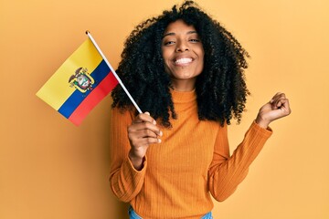 African american woman with afro hair holding ecuador flag screaming proud, celebrating victory and success very excited with raised arm