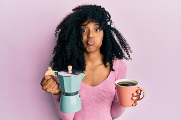 African american woman with afro hair drinking italian coffee puffing cheeks with funny face. mouth inflated with air, catching air. - obrazy, fototapety, plakaty