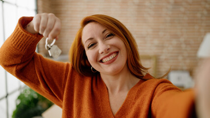 Young redhead woman making selfie by the camera holding key of new house at new home