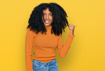 Young african american girl wearing casual clothes smiling with happy face looking and pointing to the side with thumb up.