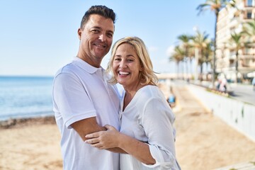 Obraz premium Middle age man and woman couple hugging each other standing at seaside