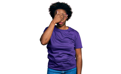 African american woman with afro hair wearing casual purple t shirt covering eyes with hand, looking serious and sad. sightless, hiding and rejection concept